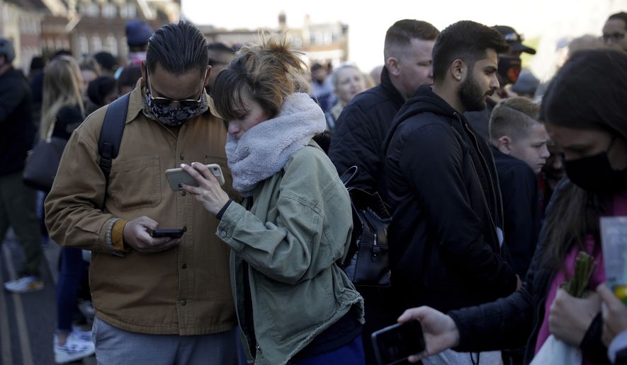 People watch live coverage on their phones as they gather outside Windsor Castle during the funeral of Britain's Prince Philip in Windsor, England, Saturday, April 17, 2021. Philip died April 9 at the age of 99 after 73 years of marriage to Britain's Queen Elizabeth II. Coronavirus restrictions mean there will be only 30 mourners for the service, including the widowed queen, her four children and her eight grandchildren. (AP Photo/Matt Dunham)
