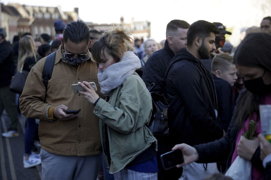 People watch live coverage on their phones as they gather outside Windsor Castle during the funeral of Britain's Prince Philip in Windsor, England, Saturday, April 17, 2021. Philip died April 9 at the age of 99 after 73 years of marriage to Britain's Queen Elizabeth II. Coronavirus restrictions mean there will be only 30 mourners for the service, including the widowed queen, her four children and her eight grandchildren. (AP Photo/Matt Dunham)