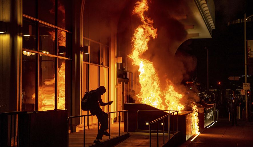 Demonstrators set fire to the front of the California Bank and Trust building during a protest against police brutality in Oakland, Calif., Friday, April 16, 2021. (AP Photo/Ethan Swope)