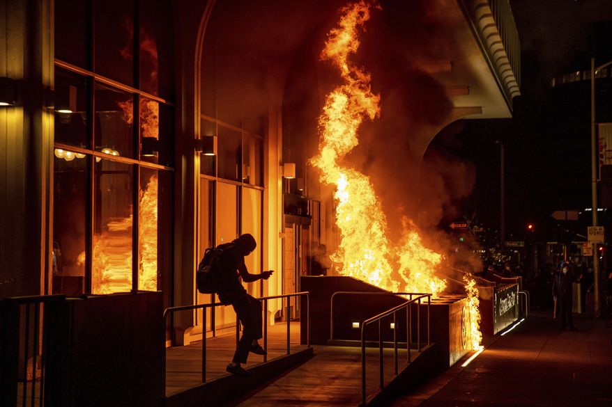 Demonstrators set fire to the front of the California Bank and Trust building during a protest against police brutality in Oakland, Calif., Friday, April 16, 2021. (AP Photo/Ethan Swope)