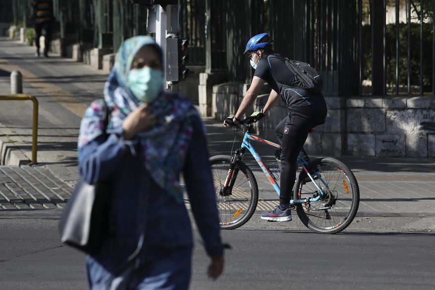 Wearing protective face masks to help prevent the spread of the coronavirus, a man rides his bicycle and a woman crosses a street in downtown Tehran, Iran, Monday, April 5, 2021. Iran's capital is once again under a code red status, the highest level of restrictions imposed to curb the spread of the coronavirus as the country struggles with a new surge in daily deaths. (AP Photo/Vahid Salemi)