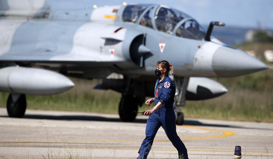 An air force officer walks as a Greek fighter jet Mirage 2000-5 taxis during the international military exercise Iniochos at Andravida air base, about 279 kilometres (174 miles) southwest of Athens, Tuesday, April 20, 2021. Greece vowed Tuesday to expand military cooperation with traditional NATO allies as well as Middle Eastern powers in a race to modernize its armed forces and face its militarily assertive neighbor Turkey. (AP Photo/Thanassis Stavrakis)