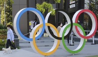 A woman with her dog walks past the Olympic rings in Tokyo, Tuesday, April 20, 2021. (AP Photo/Koji Sasahara) **FILE**