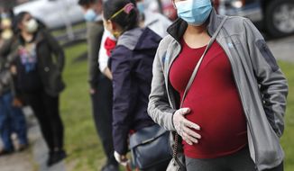 In this Thursday, May 7, 2020, photo, a pregnant woman wearing a face mask and gloves holds her belly as she waits in line for groceries with hundreds during a food pantry sponsored by Healthy Waltham for those in need due to the COVID-19 virus outbreak, at St. Mary&#39;s Church in Waltham, Mass. (AP Photo/Charles Krupa) **FILE**