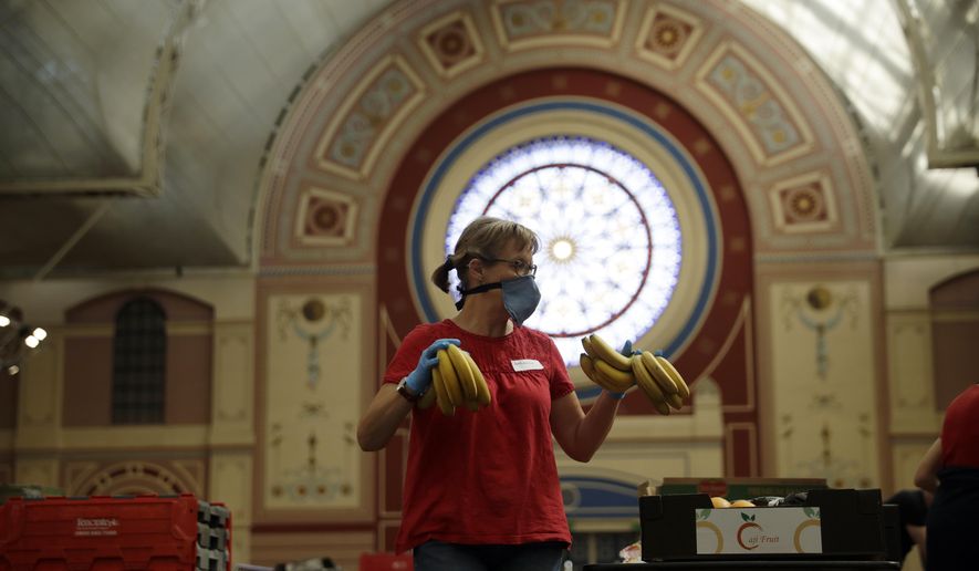 FILE - In this Tuesday, April 21, 2020 file photo, a volunteer for the Edible London food project checks and packs bananas to be put in food packs and delivered to residents who need it in the Haringey Council area, at a hub setup as a result of coronavirus inside the Alexandra Palace venue, in north London. A charity says U.K. food bank rose by a third during the past 12 months as the COVID-19 pandemic left more people without the money to buy basic necessities. The Trussell Trust said Thursday, April 22, 2021 that the food banks it works with handed out more than 2.5 million food parcels in the year through March, up from 1.9 million a year earlier. (AP Photo/Matt Dunham, File)