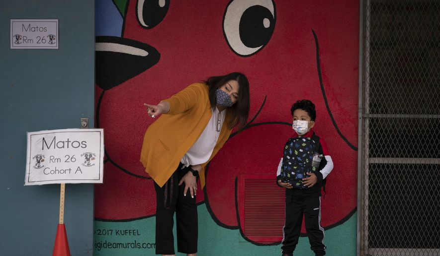 FILE - In this April 13, 2021, file photo, kindergarten teacher Lilia Matos and her student Jesus Mendez stand outside their classroom on the first day of in-person learning at Heliotrope Avenue Elementary School in Maywood, Calif. California's public schools have seen a "sharp decline" in enrollment this year as the pandemic forced millions into online school and districts dawdled in bringing children back to the classroom. Data from the California Department of Education released Thursday, April 22, 2021, shows the number of students at K-12 schools dropped by more than 160,000 this academic year, most of them in K-6. (AP Photo/Jae C. Hong, File)