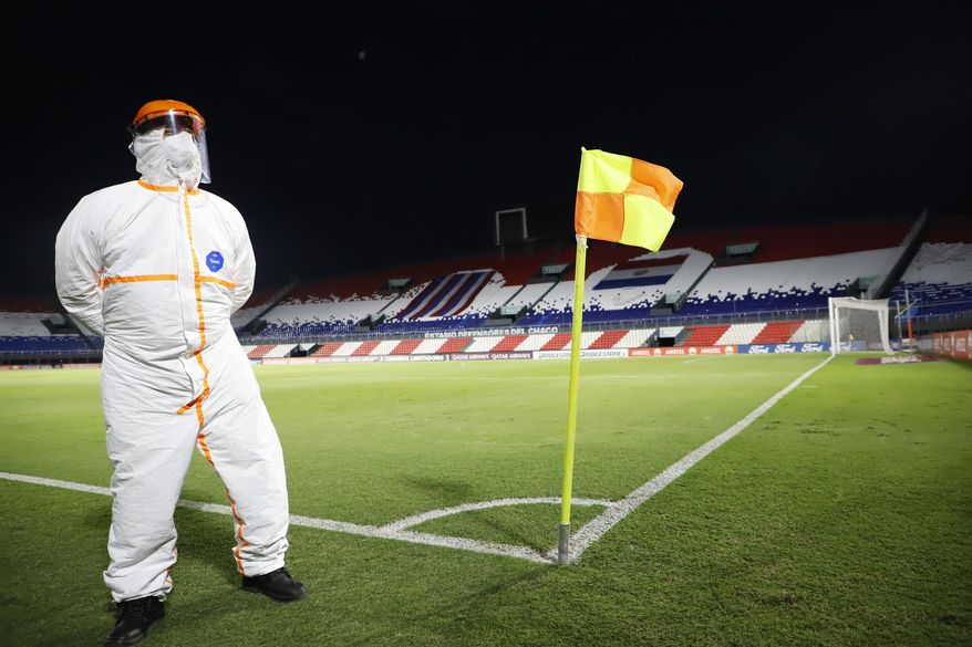 A Conmebol worker, wearing protective gear due to COVID-19, stands guard on the pitch inside "Defensores del Chaco" Stadium before the start of a Copa Libertadores soccer match between Brazil's Gremio and Ecuador's Independiente del Valle in Asuncion, Paraguay, Friday, April 9, 2021. (Natalia Aguilar/Pool via AP)