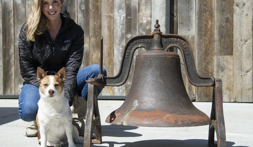 Morgan Stuart and her dog, Bowser, sit next to the Gallatin Gateway School bell on April 21, 2021, in Gallatin Gateway, Mont., that was recovered from Karen ter Telgte after her husband, Ed ter Telgte, took it down in the 1970′s. (Rachel Leathe/Bozeman Daily Chronicle via AP)