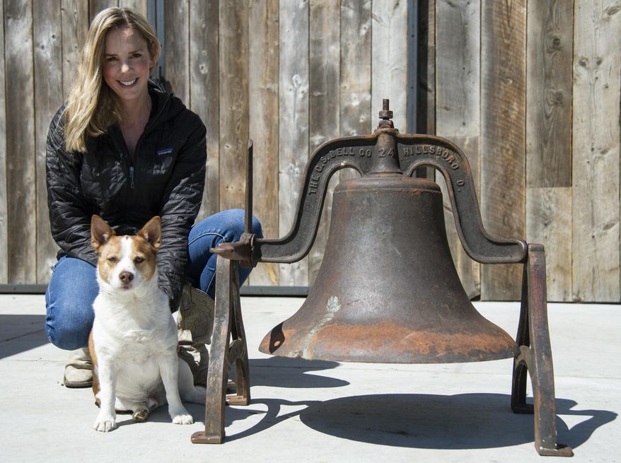 Morgan Stuart and her dog, Bowser, sit next to the Gallatin Gateway School bell on April 21, 2021, in Gallatin Gateway, Mont., that was recovered from Karen ter Telgte after her husband, Ed ter Telgte, took it down in the 1970′s. (Rachel Leathe/Bozeman Daily Chronicle via AP)