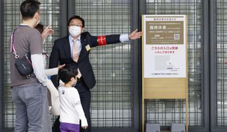 An usher briefs visitors at an entrance of a department store which is open partially, in Tokyo Sunday, April 25, 2021. Japan’s department stores, bars and theaters shuttered Sunday, as the government “state of emergency” over the coronavirus pandemic kicked in amid growing worries about a surge in infections. (Hiroko Harima/Kyodo News via AP)