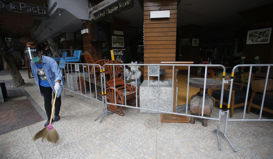 A worker wearing a face mask to help curb the spread of the coronavirus sweeps with a broom around a restaurant in Khao San road, a popular hangout for Thais and tourists in Bangkok, Thailand, Monday, April 26, 2021. Cinemas, parks and gyms were among venues closed in Bangkok as Thailand sees its worst surge of the pandemic. A shortage of hospital beds, along with a failure to secure adequate coronavirus vaccine supplies, have pushed the government into imposing the new restrictions. (AP Photo/Anuthep Cheysakron)