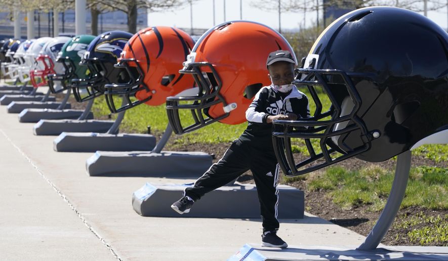 Joseph Toliver, 4, plays on one of the 32 NFL team helmets on display, Tuesday, April 13, 2021, in downtown Cleveland. Forced to cancel last year&#39;s NFL Draft in Las Vegas, the league is using lessons learned while plowing through an unprecedented, socially-distanced 2020 season and holding the Super Bow in Tampa, to have a draft that will look much more like normal — well, the new normal — with fans wearing their favorite team&#39;s colors and required masks.(AP Photo/Tony Dejak) **FILE**