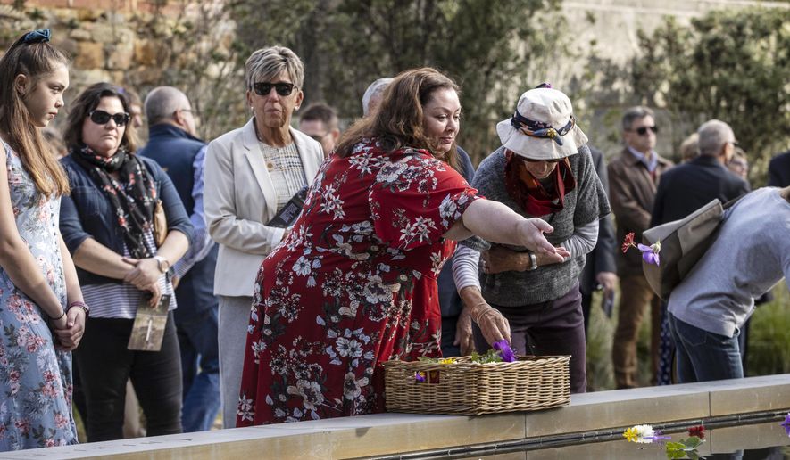 Gaye Myler, center, throws a flower into a reflection pool at Port Arthur, Australia, Wednesday, April 28, 2021, as Australia marks the 25th anniversary of a lone gunman killing 35 people in Tasmania state in a massacre that galvanized the nation into tightening gun laws. (Luke Bowden/Pool via AP)