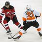 The puck flies in front of New Jersey Devils defenseman Ryan Murray (22) with Philadelphia Flyers center Scott Laughton (21) watching during the second period of an NHL hockey game Thursday, April 29, 2021, in Newark, N.J. (AP Photo/Kathy Willens)