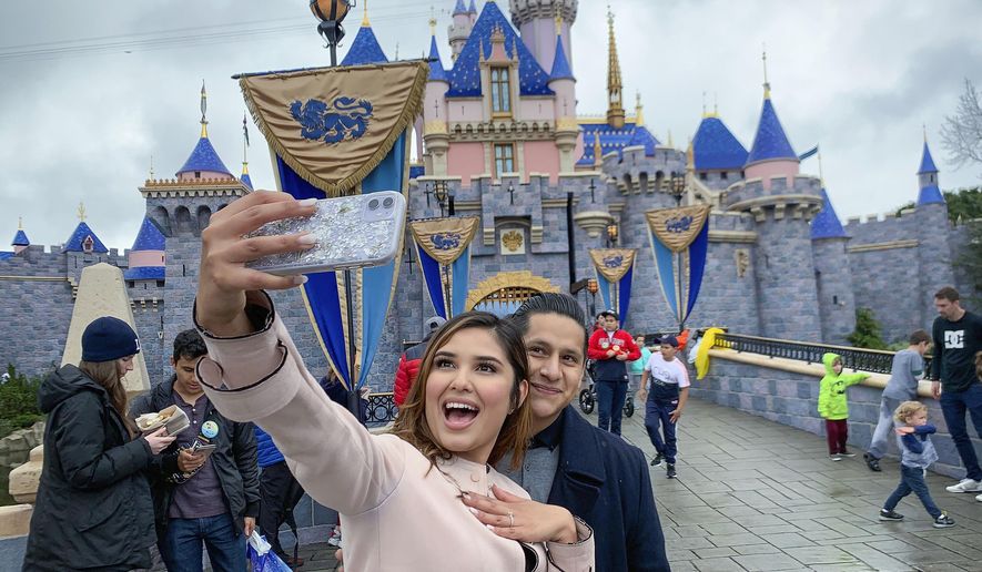 FILE - In this March 13, 2020, file photo, Katherine Quezada shows off her engagement ring as she takes a selfie with her new fiance, Fernando Carranza, in front of Sleeping Beauty Castle the during the last day before Disneyland closes because of the COVID-19 coronavirus outbreak, in Anaheim, Calif. Carranza proposed to Quezada in front of the castle earlier that day. Disneyland Park and Disney California Adventure park will reopen to visitors on Friday, April 30, 2021. (Jeff Gritchen/The Orange County Register via AP, File)