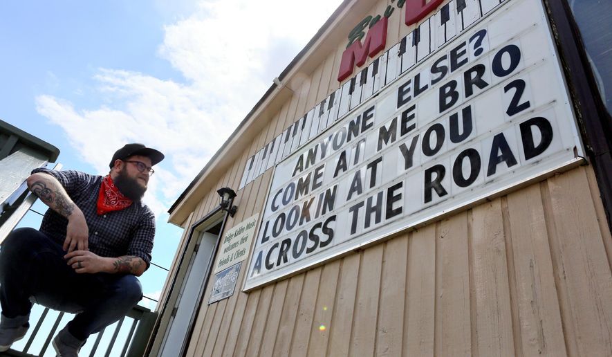Jim Bohon a music instructor with Bridge Kaldro Music got his sign back and is having fun, poking fun, at the store's retail neighborhood in Christiansburg, Va., Thursday, April 22, 2021. It was Bridge Kaldro Music that that touched off this battle royale, challenging businesses to poke silly fun at one another. It has quickly spread across town and gone viral online. (Matt Gentry/The Roanoke Times via AP)