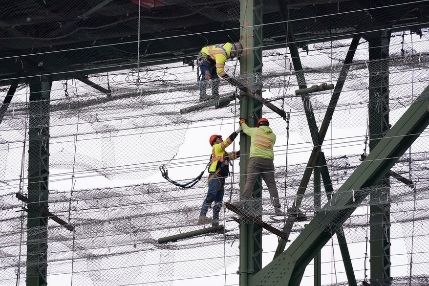 Workers stand on wire mesh below the decking of the Deception Pass Bridge, nearly 1,000-feet long and about 180-feet above the waters below, as work to replace corroded steel and paint the structure continues Thursday, April 29, 2021, in Deception Pass, Wash. (AP Photo/Elaine Thompson) ** FILE **
