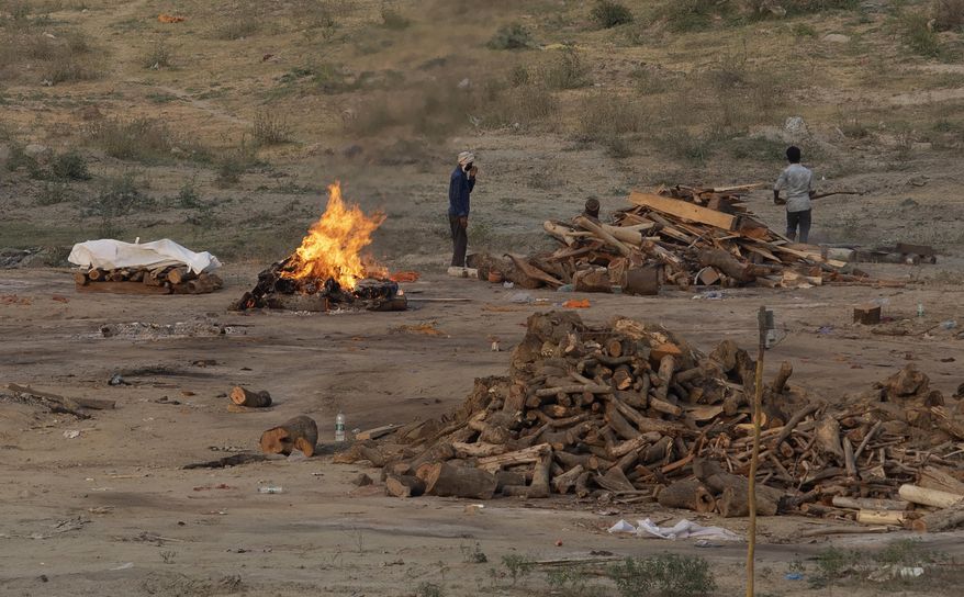 Body of a COVID-19 victim lies covered in white cloth next to a burning pyre of another victim at a cremation ground in Prayagraj, India, Saturday, May 1, 2021. India on Saturday set yet another daily global record with 401,993 new cases, taking its tally to more than 19.1 million. Another 3,523 people died in the past 24 hours, raising the overall fatalities to 211,853, according to the Health Ministry. Experts believe both figures are an undercount. (AP Photo/Rajesh Kumar Singh)
