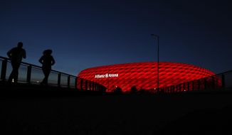 FILE-In this March 16, 2020 taken photo jogger make their way after the sun sets at the &#39;Allianz Arena&#39; soccer stadium in Munich, Germany. European ruling body UEFA said on Friday the German city of Munich will remain as one of the Euro 2020 host cities. The confirmation came during a UEFA executive board videoconference after the federation was informed by local authorities that all four matches in Munich will be able to welcome a minimum of 14,500 spectators. (AP Photo/Matthias Schrader)