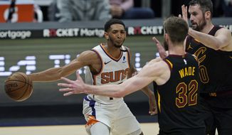 Phoenix Suns&#x27; Cameron Payne, left, passes around Cleveland Cavaliers&#x27; Dean Wade and Kevin Love in the first half of an NBA basketball game, Tuesday, May 4, 2021, in Cleveland. (AP Photo/Tony Dejak)