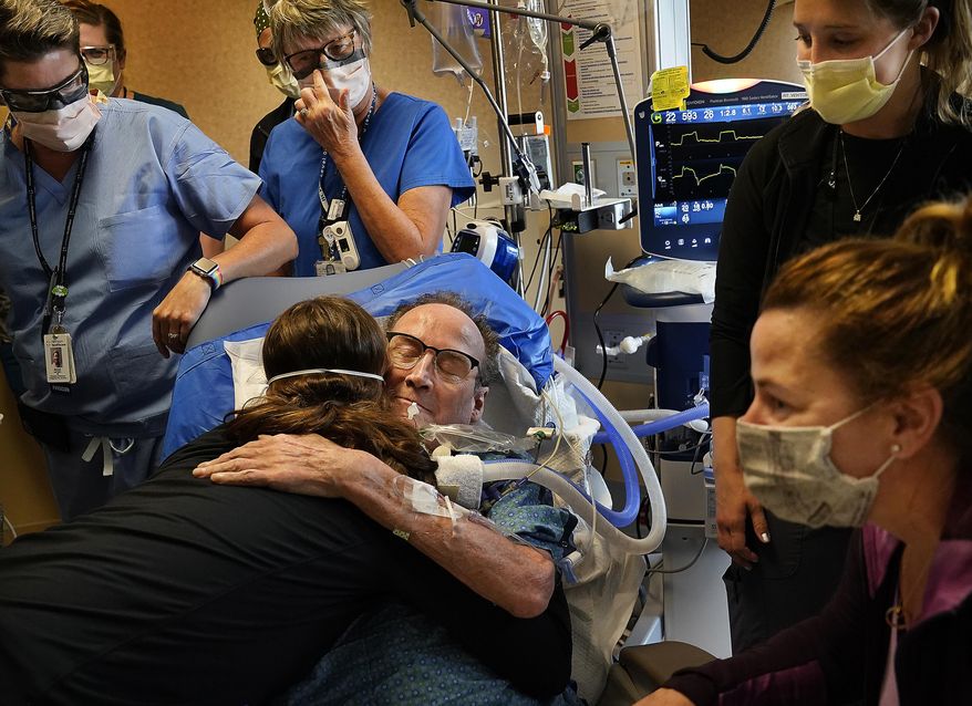 In this May 3, 2021, file photo, Hennepin County Medical Center patient John Grubb, of St. Michael, hugs and says goodbye to several of his caregivers as his wife, Kelly, lower right, looks on before he is discharged from the hospital in Minneapolis, after spending 81 days on the ECMO heart-lung bypass machine, which has been the treatment of last resort in COVID-19 care. (David Joles/Star Tribune via AP, File)