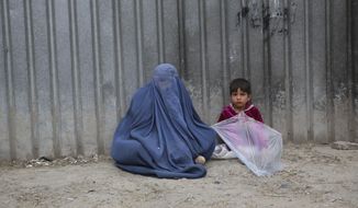 In this May 2, 2020 file photo, a woman waits to receive alms with her daughter during the Muslim fasting month of Ramadan, in Kabul, Afghanistan. (AP Photo/Rahmat Gul, File)  **FILE**