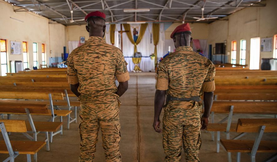 Two soldiers stand in the Catholic church at the 10th RCAS army barracks in Kaya, Burkina Faso, Saturday, April 10, 2021. Once considered a beacon of peace and religious coexistence in the region, the West African nation has been embroiled in unprecedented violence linked to al-Qaida and the Islamic State since 2016, throwing an ill-equipped and undertrained army into disarray — and overwhelming the chaplains tasked with supporting them. (AP Photo/Sophie Garcia)