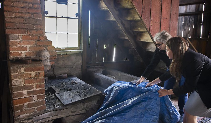 Barbara Fromer, who has owned the property since 1984, left and Jean LaPadula, Main Street coordinator and grant manager, pull a tarp off the original blacksmiths fire box and forge in a historic blacksmith shop in New Market, Md., building. on April 29, 2021. The shop that appeared destined for demolition may be saved and renewed as a tourist attraction after town leaders and the property’s owner dug into details of the structure’s past. (Bill Green/The Frederick News-Post via AP)