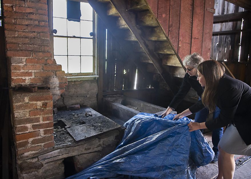 Barbara Fromer, who has owned the property since 1984, left and Jean LaPadula, Main Street coordinator and grant manager, pull a tarp off the original blacksmiths fire box and forge in a historic blacksmith shop in New Market, Md., building. on April 29, 2021. The shop that appeared destined for demolition may be saved and renewed as a tourist attraction after town leaders and the property’s owner dug into details of the structure’s past. (Bill Green/The Frederick News-Post via AP)