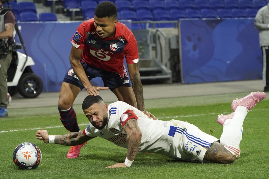 Lyon&#39;s Memphis Depay, down, challenges for the ball with Lille&#39;s Reinildo Isnard Mandava, up, during their French League One soccer match in Decines, near Lyon, central France, Sunday, April 25, 2021. (AP Photo/Laurent Cipriani)