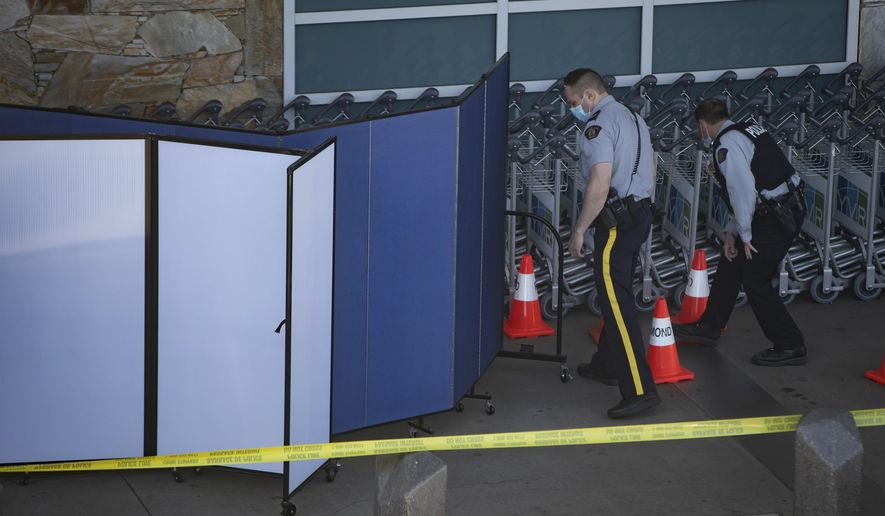 Royal Canadian Mounted Police officers search around rows of luggage carts as screens block off an area of the sidewalk after a shooting outside the international departures terminal at Vancouver International Airport, in Richmond, British Columbia, Sunday, May 9, 2021. (Darryl Dyck/The Canadian Press via AP)