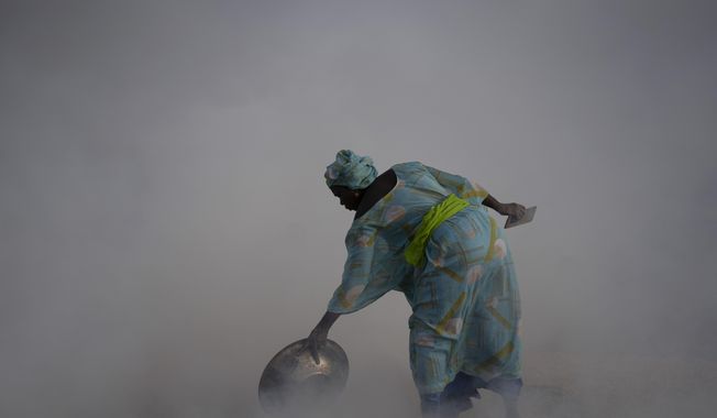 Ndeye Yacine Dieng drops embers over peanut shells covering fish as she walks amidst the smoke on Bargny beach, some 35 kilometers (22 miles) east of Dakar, Senegal, Wednesday April 21, 2021. Since her birth on Senegal&#x27;s coast, the ocean has always given Ndeye Yacine Dieng life. Her grandfather was a fisherman, and her grandmother and mother processed fish. Like generations of women, she helps support her family in the small community of Bargny by drying, smoking, salting and fermenting the catch brought home by male villagers. They were baptized by fish, these women say. (AP Photo/Leo Correa)