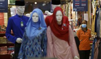 In this Saturday, April 24, 2021, photo, a clothing shop clerk wearing a protective mask waits for customers at the Ramadan bazaar in Kuala Lumpur, Malaysia. Malaysian Prime Minister Muhyiddin Yassin announced Monday that the whole country will be placed under a near lockdown for about a month but all economic sectors will be allowed to operate. (AP Photo/Vincent Thian)