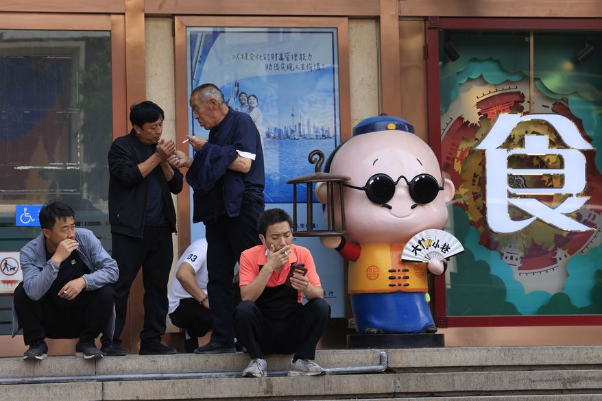 Residents smoke along the popular Wangfujing shopping district in Beijing Tuesday, May 11, 2021. The number of working-age people in China fell over the past decade as its aging population barely grew, a census showed Tuesday, adding to economic challenges for Chinese leaders who have ambitious strategic goals. (AP Photo/Ng Han Guan)