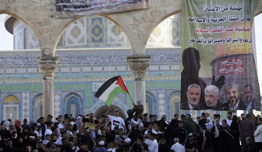 A banner depicting Hamas leadership hangs on an archway as Muslims gather following Eid al-Fitr prayers at the Dome of the Rock Mosque in the Al-Aqsa Mosque compound in the Old City of Jerusalem, Thursday, May 13, 2021. Eid al-Fitr, festival of breaking of the fast, marks the end of the holy month of Ramadan. (AP Photo/Mahmoud Illean)