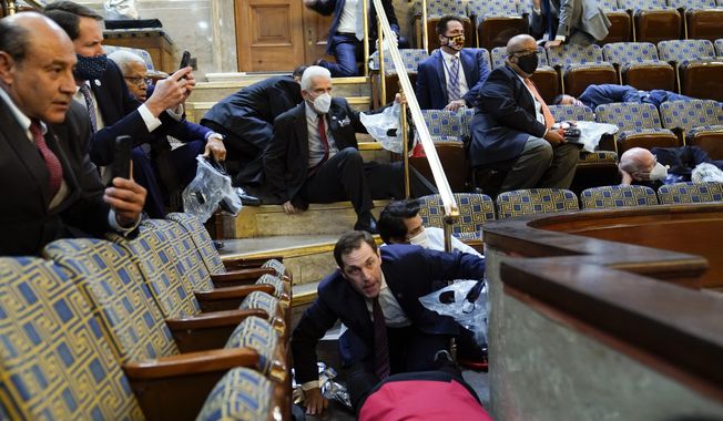 In this Jan. 6, 2021, file photo, people shelter in the House chamber as rioters try to break into the House Chamber at the U.S. Capitol in Washington. (AP Photo/Andrew Harnik, File)