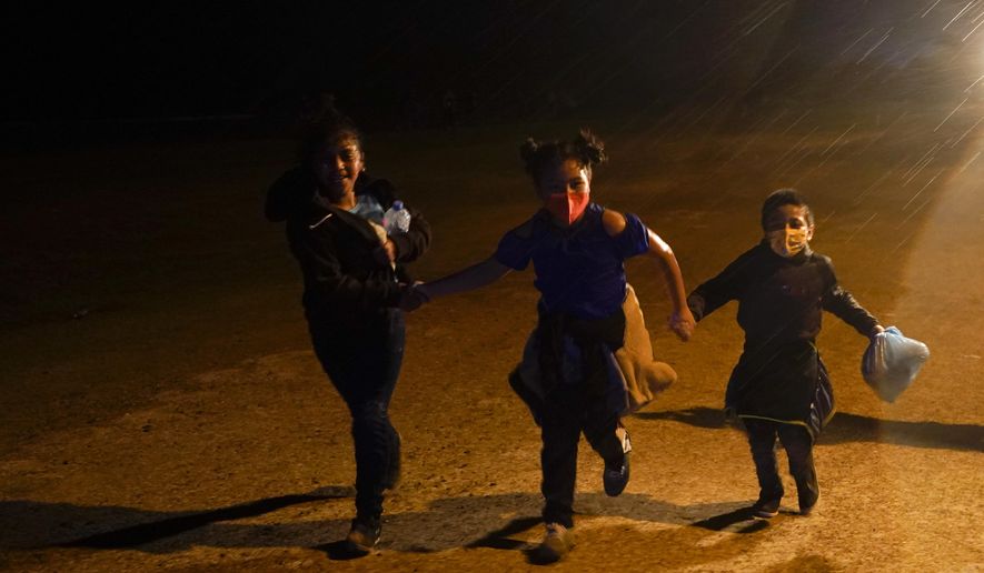 Three young migrants hold hands as they run in the rain at an intake area after turning themselves in upon crossing the U.S.-Mexico border Tuesday, May 11, 2021, in Roma, Texas. The number of unaccompanied children encountered on the U.S. border with Mexico in April eased from an all-time high a month earlier, while more adults were found coming without families, authorities said Tuesday. (AP Photo/Gregory Bull) **FILE**