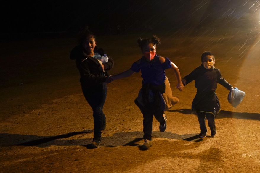 Three young migrants hold hands as they run in the rain at an intake area after turning themselves in upon crossing the U.S.-Mexico border Tuesday, May 11, 2021, in Roma, Texas. The number of unaccompanied children encountered on the U.S. border with Mexico in April eased from an all-time high a month earlier, while more adults were found coming without families, authorities said Tuesday. (AP Photo/Gregory Bull) **FILE**