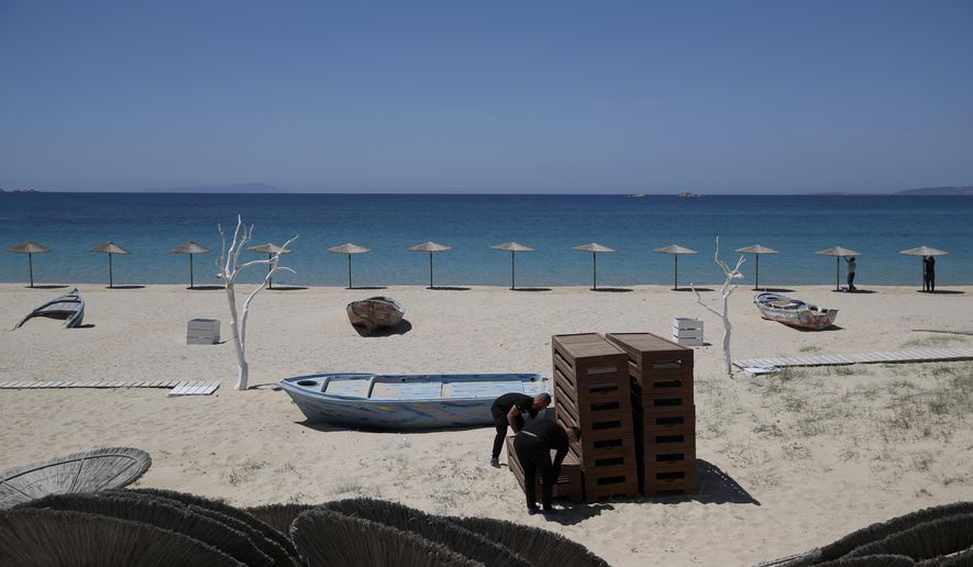 Workers arrange sunbeds as others install umbrellas at Plaka beach on the Aegean island of Naxos, Greece, Wednesday, May 12, 2021. With debts piling up, southern European countries are racing to reopen their tourism services despite delays in rolling out a planned EU-wide travel pass. Greece Friday became the latest country to open up its vacation season as it dismantles lockdown restrictions and focuses its vaccination program on the islands. (AP Photo/Thanassis Stavrakis)