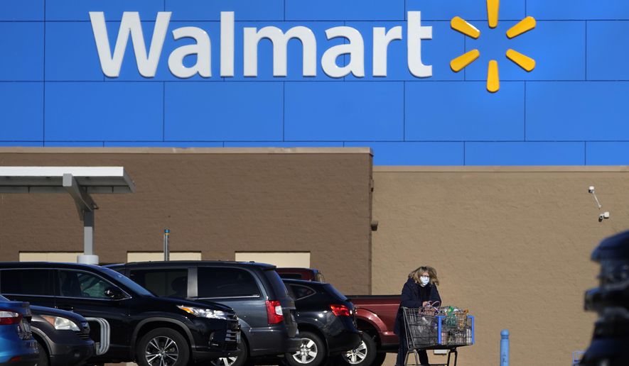 In this Nov. 18, 2020 file photo, a woman, wearing a protective face mask due to the COVID-19 virus outbreak, wheels a cart with her purchases out of a Walmart store, in Derry, N.H. Walmart, the world’s largest retailer, said Friday, May 14, 2021 that it won’t require vaccinated shoppers or workers to wear a mask in its U.S. stores, unless state or local laws say otherwise. Vaccinated shoppers can go maskless immediately, the company said. Vaccinated workers can stop wearing them on May 18. (AP Photo/Charles Krupa, File)