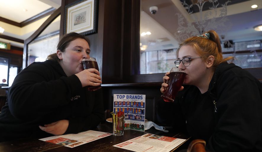 Libby Jones, right, with her colleague Shannon Maiden, both nurses from Great Ormond Street hospital who have just finished an overnight shift, have a pint of cider at the Shakespeare's Head pub, which will be reopening for the first time to serve indoor customers since the end of the latest coronavirus lockdown, in London, Monday, May 17, 2021. (AP Photo/Alastair Grant)