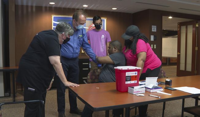 In this image made from video, a health care professional and representatives of JARC, a nonprofit dedicated to assisting those with developmental disabilities, try to persuade Noah Lebon to take a COVID-19 vaccine shot on Thursday, May 20, 2021, in Bloomfield Hills, Mich. Noah&#x27;s mother, LaQuae Lebon, is standing beside her son in the vaccine clinic. (AP Photo/Mike Householder)