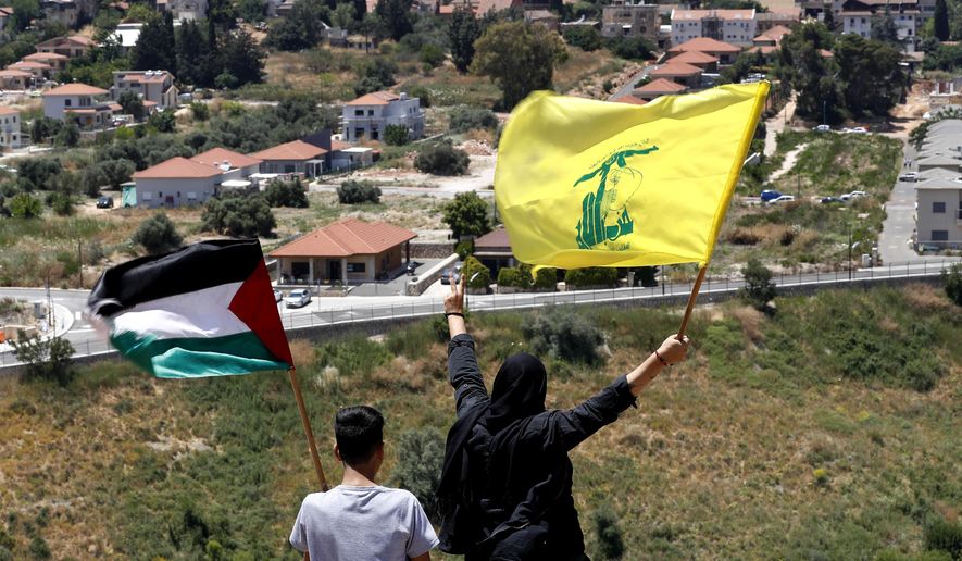 In this May 15, 2021, file photo, Lebanese wave Hezbollah and Palestinian flags, as they stand in front of the Israeli town of Metula, background, on the Lebanese side of the Lebanese-Israeli border in the southern village of Kfar Kila, Lebanon. Lebanon&#39;s Hezbollah militia looms large over the current Israel-Hamas war, even though it has stayed out of the fighting so far. Hezbollah&#39;s firepower is far greater than that of Gaza&#39;s Hamas rulers, and Israel keeps a wary eye on its northern border for any signs Hezbollah might get off the sidelines. (AP Photo/Hussein Malla, File)