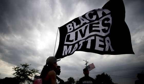 Estephanie Ward, 29, of Flint, Mich., stands alongside other Black Lives Matter supporters waving the flag through the wind as protesters demonstrate along Miller Road outside of a Target, Tuesday, May 25, 2021, in Flint Township, one year after the death of George Floyd. (Jake May/The Flint Journal via AP) ** FILE **