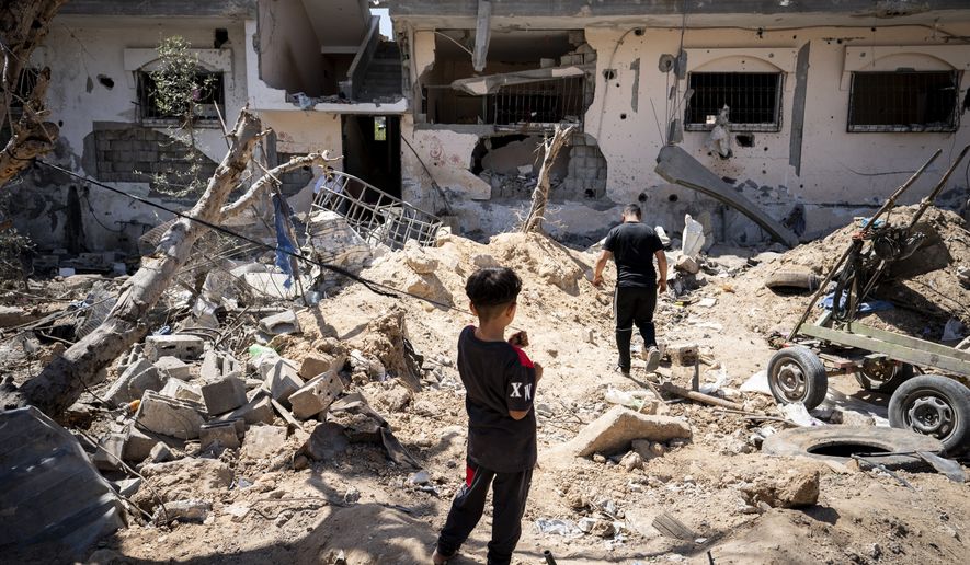 People stand in a clearing strewn with debris from an israeli airstrike during an 11-day war between Gaza&#39;s Hamas rulers and Israel, Wednesday, May 26, 2021, in Beit Hanoun, Gaza Strip. (AP Photo/John Minchillo)