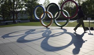 A woman walks by the Olympic Rings near the National Stadium in Tokyo Wednesday, June 9, 2021. Roads were being closed off since last Tuesday around Tokyo Olympic venues, including the new $1.4 billion National Stadium where the opening ceremony is set for July 23.(AP Photo/Eugene Hoshiko)