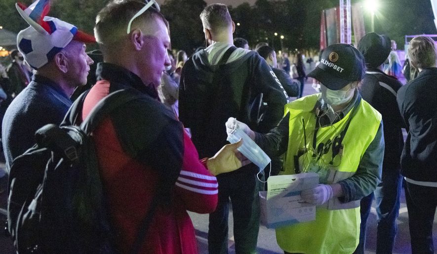A member of the security personnel distributes face masks as supporters of Russia's team watch the Euro 2020 soccer championship group B match between Russia and Belgium at a fan area in the Luzhniki Olympic Complex in Moscow, Russia, Saturday, June 12, 2021. (AP Photo/Pavel Golovkin)