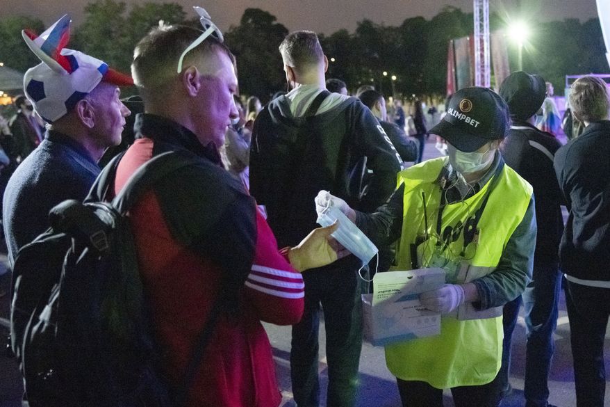 A member of the security personnel distributes face masks as supporters of Russia's team watch the Euro 2020 soccer championship group B match between Russia and Belgium at a fan area in the Luzhniki Olympic Complex in Moscow, Russia, Saturday, June 12, 2021. (AP Photo/Pavel Golovkin)