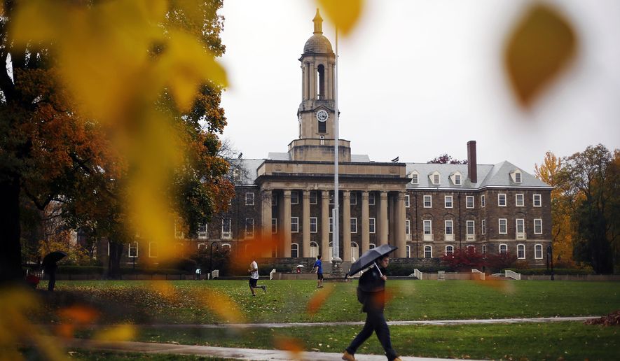 In this Oct. 28, 2015 file photo, a Penn State student walks in the rain past Old Main on the Penn State main campus in State College, Pa. Lawmakers are trying to stop 144 cities across the U.S. from losing their designations as “metropolitan areas” because the federal government is upgrading the standard from a minimum of 50,000 residents in its core to a minimum of 100,000 people. State College is among the cities at risk of losing the designation. (AP Photo/Gene J. Puskar, File)