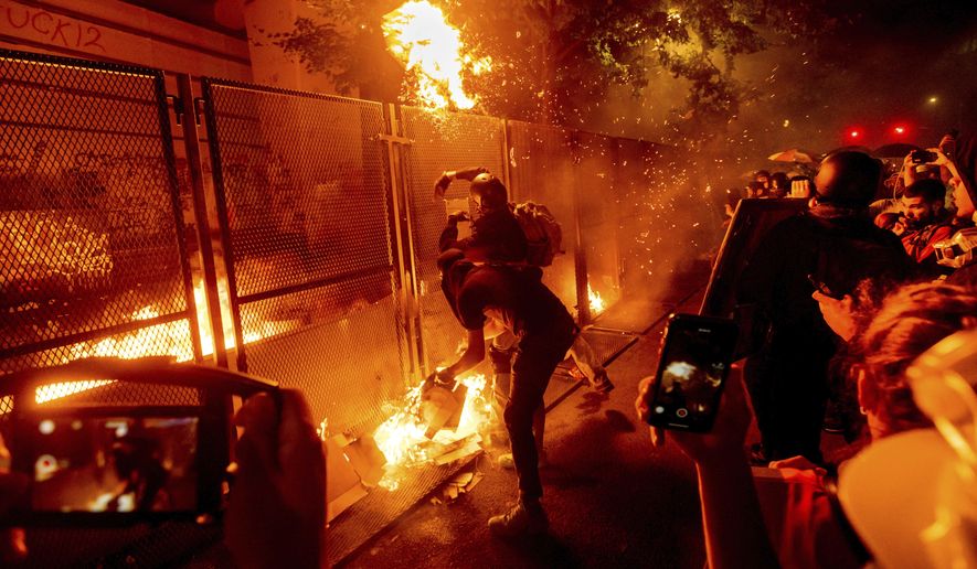 In this July 22, 2020, file photo, protesters throw flaming debris over a fence at the Mark O. Hatfield United States Courthouse in Portland, Ore. Until a year ago, the city was best known nationally for its ambrosial food scene, craft breweries and “Portlandia” hipsters. Now, months-long protests following the killing of George Floyd, a surge in deadly gun violence, and an increasingly visible homeless population have many questioning whether Oregon’s largest city can recover. (AP Photo/Noah Berger)